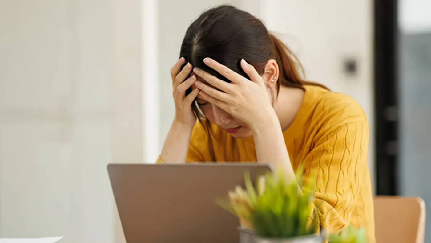 Young woman stressed at the computer with her head in her hands